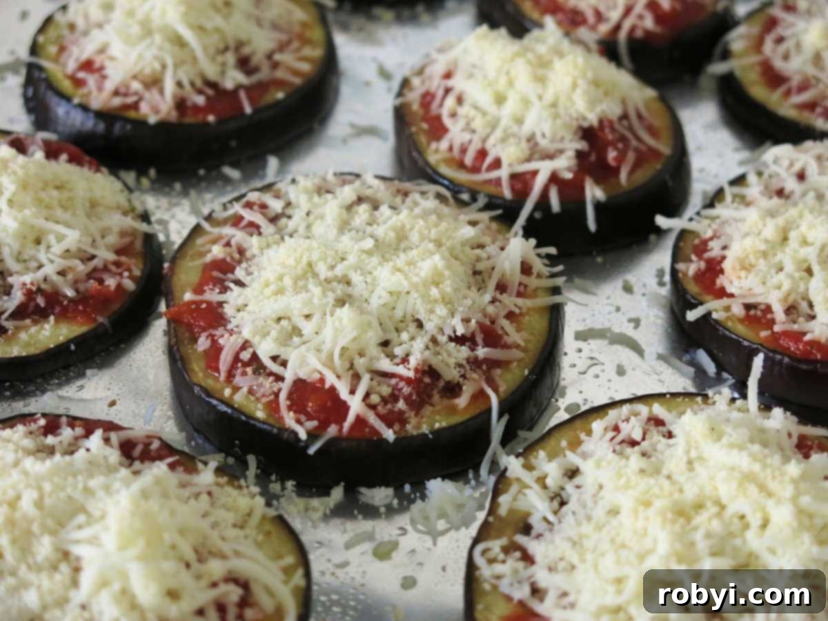 Eggplant parmesan rounds topped with marinara, mozzarella, and Parmesan cheese before cooking.