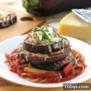 Eggplant Parmesan Stack on a white plate with an eggplant and triangle of Parmesan cheese behind it.