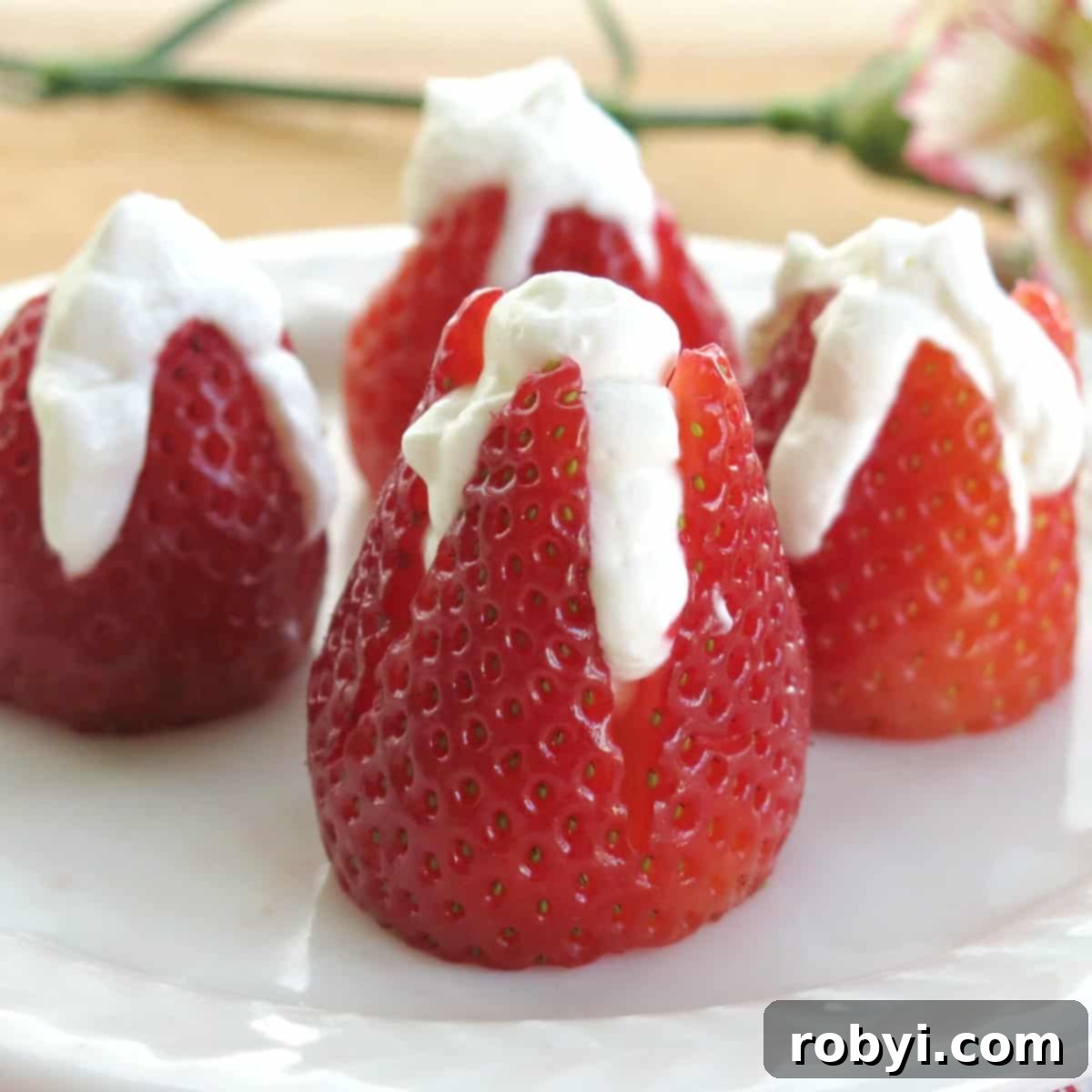 4 cheesecake stuffed strawberries on plate with flower behind it.