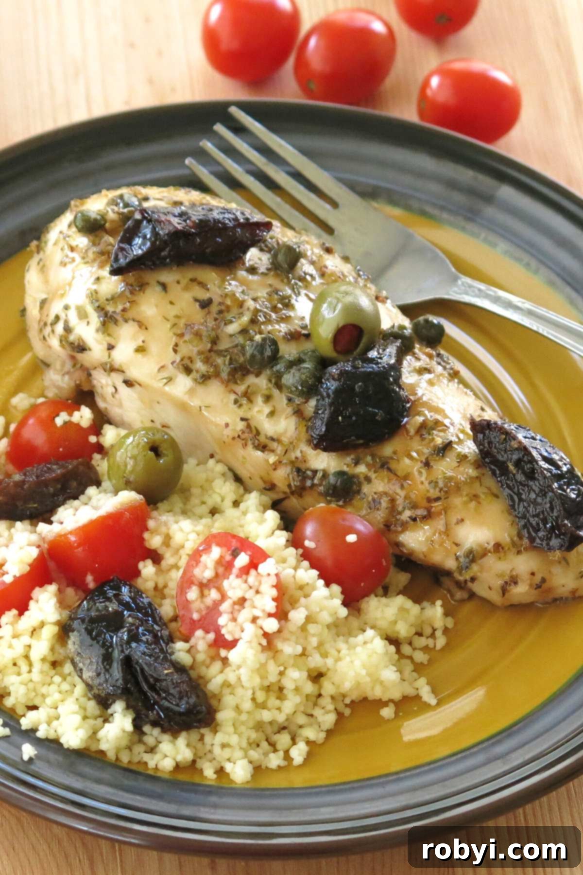 Plate with chicken marbella made with boneless breasts topped with prunes, green olives, and capers with couscous next to it.