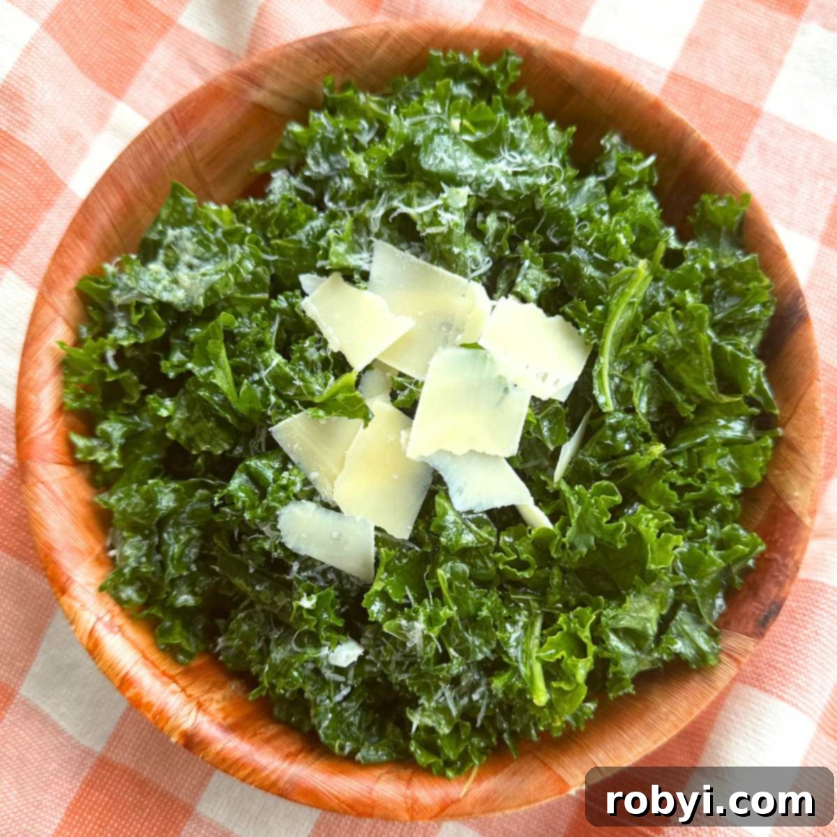 Massaged kale salad topped with shaved Parmesan and lemon dressing in a brown bowl on a orange checkered background.