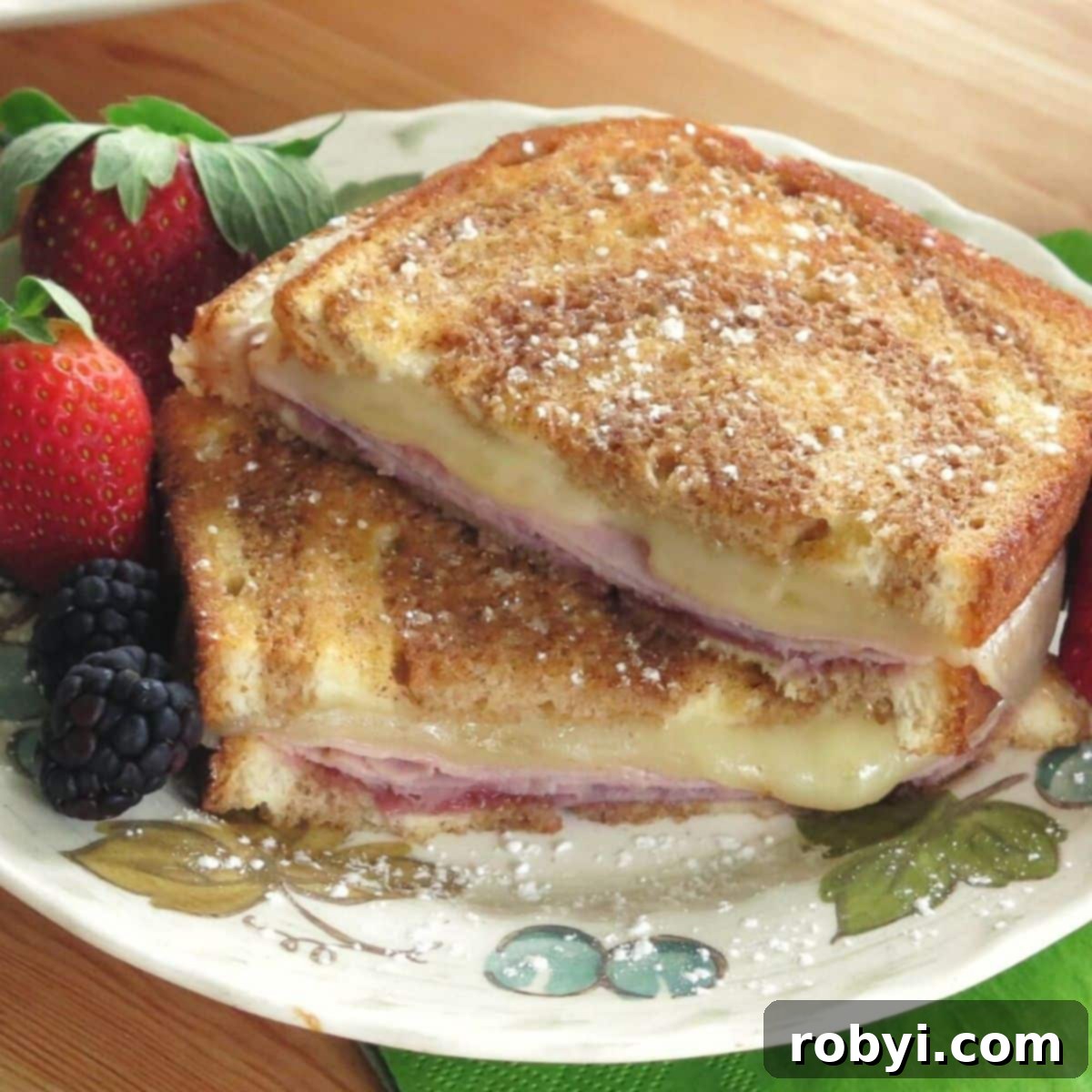 Monte Cristo Grilled Cheese: Sweet, Savory, and Jam-Stuffed 2 A perfectly golden Monte Cristo Grilled Cheese sandwich, lightly dusted with powdered sugar, resting on a plate alongside fresh raspberries and blackberries. The rich filling of ham, Swiss cheese, and raspberry jam promises a delightful sweet and savory experience.