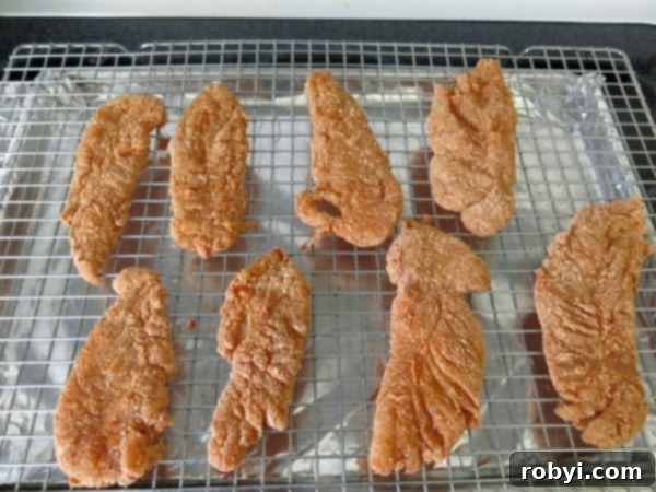 Chicken tenders coated with paprika Parmesan breading on baking rack, ready for the oven.