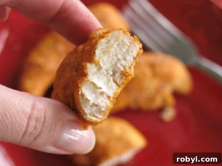 Hand holding a cooked Paprika Parmesan Chicken Nugget from an air fryer, with a bite taken to show the juicy white interior.