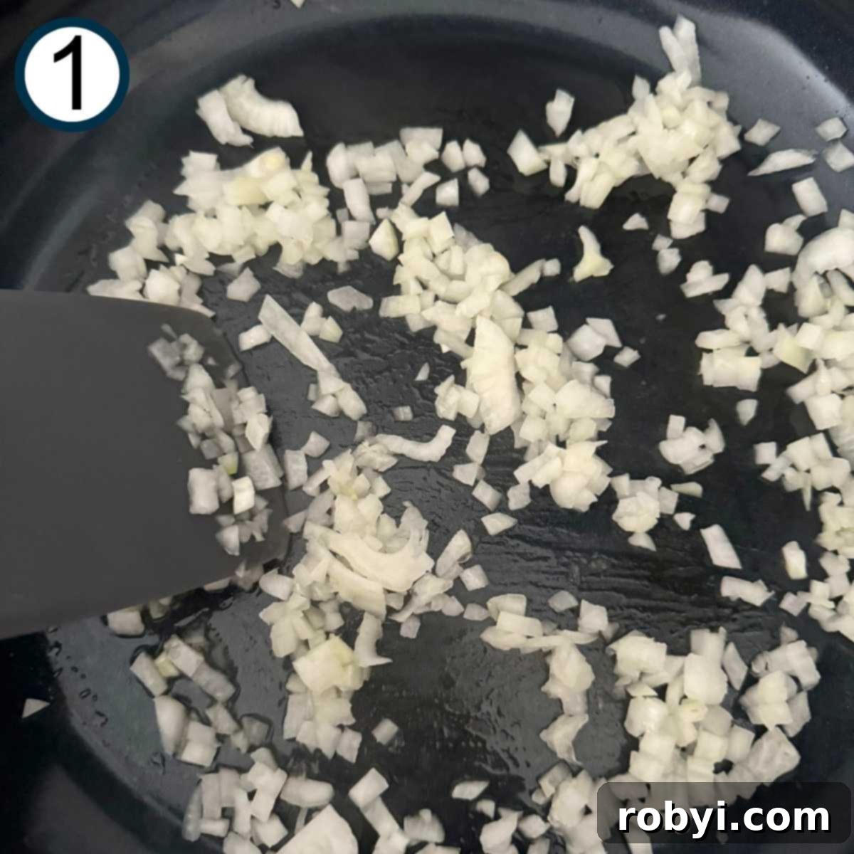 Diced onion and minced garlic sautéing in a large skillet with a spatula.
