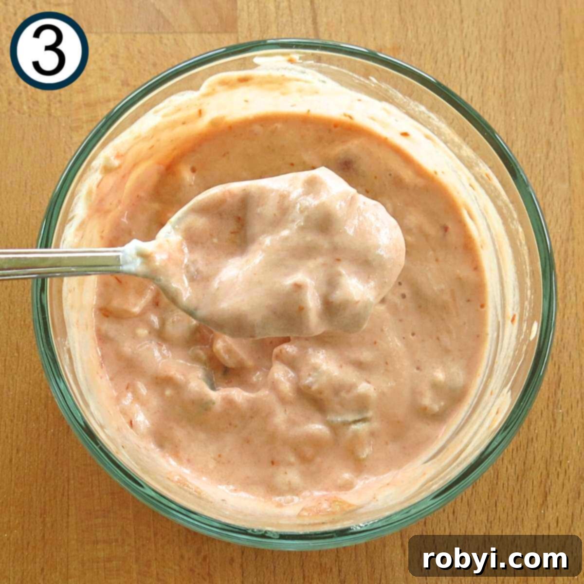 A spoon lifting a mixture of Greek yogurt and salsa from a small glass bowl, showing the creamy texture of the sauce.