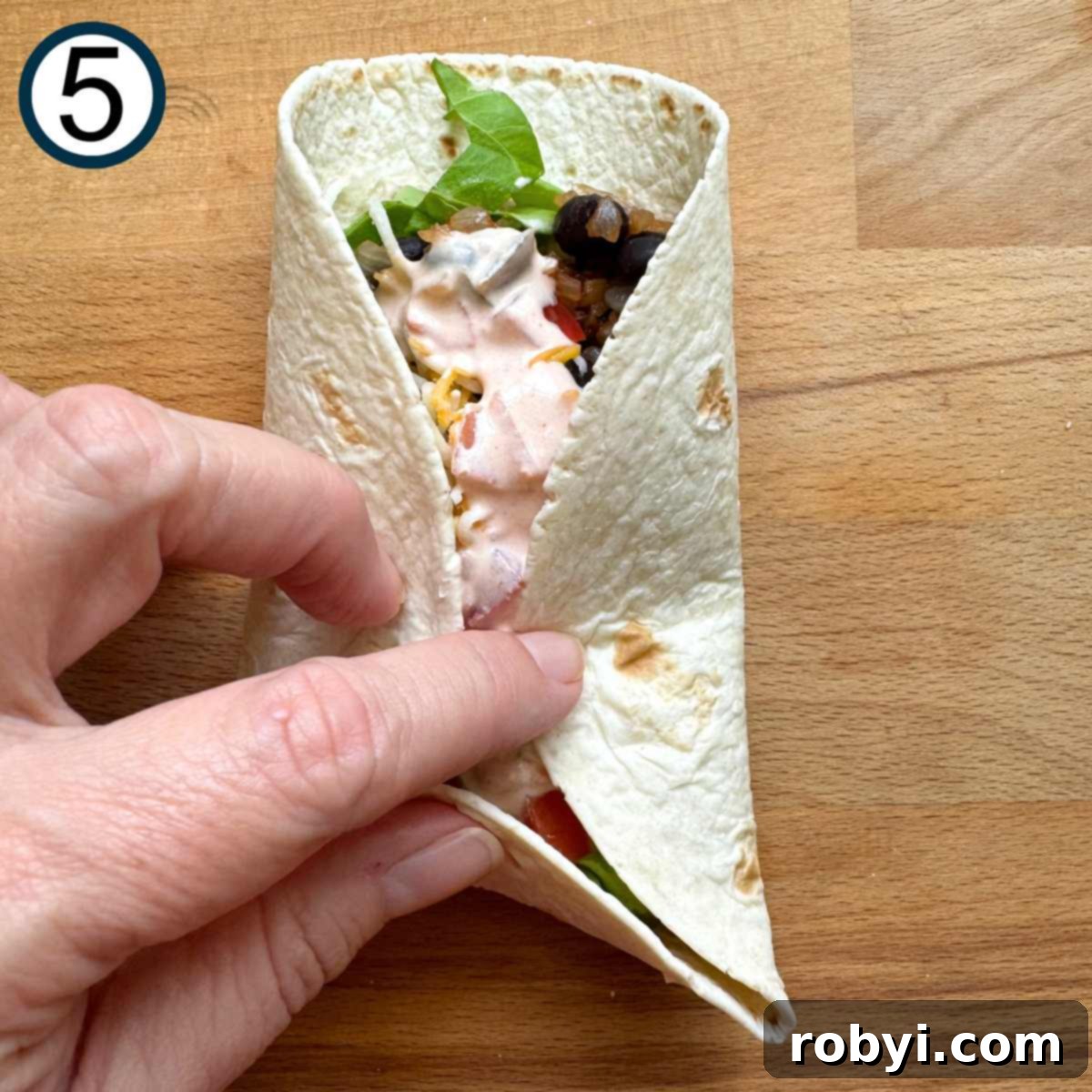 A hand demonstrating how to roll a flour tortilla wrap, by folding up the bottom edge first, then bringing the sides together to enclose the filling.