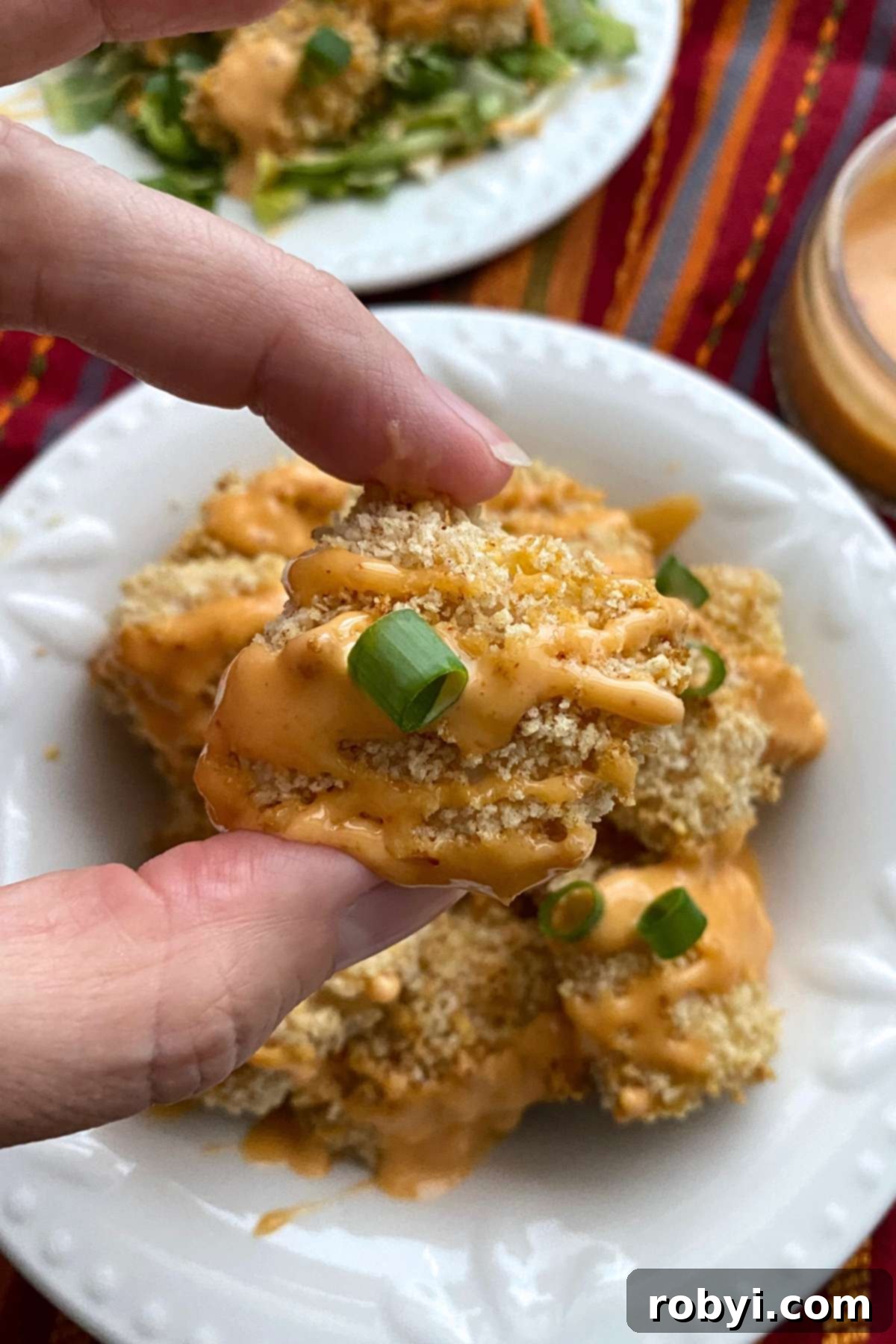 Fingers holding a nugget of baked bang bang chicken.