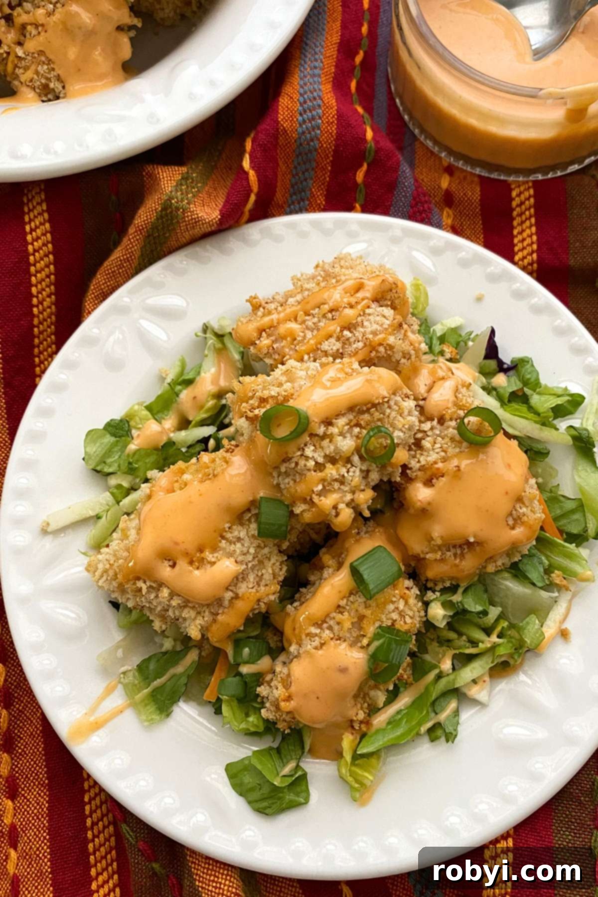 Baked bang bang chicken drizzled with sauce on a plate of crispy salad greens.