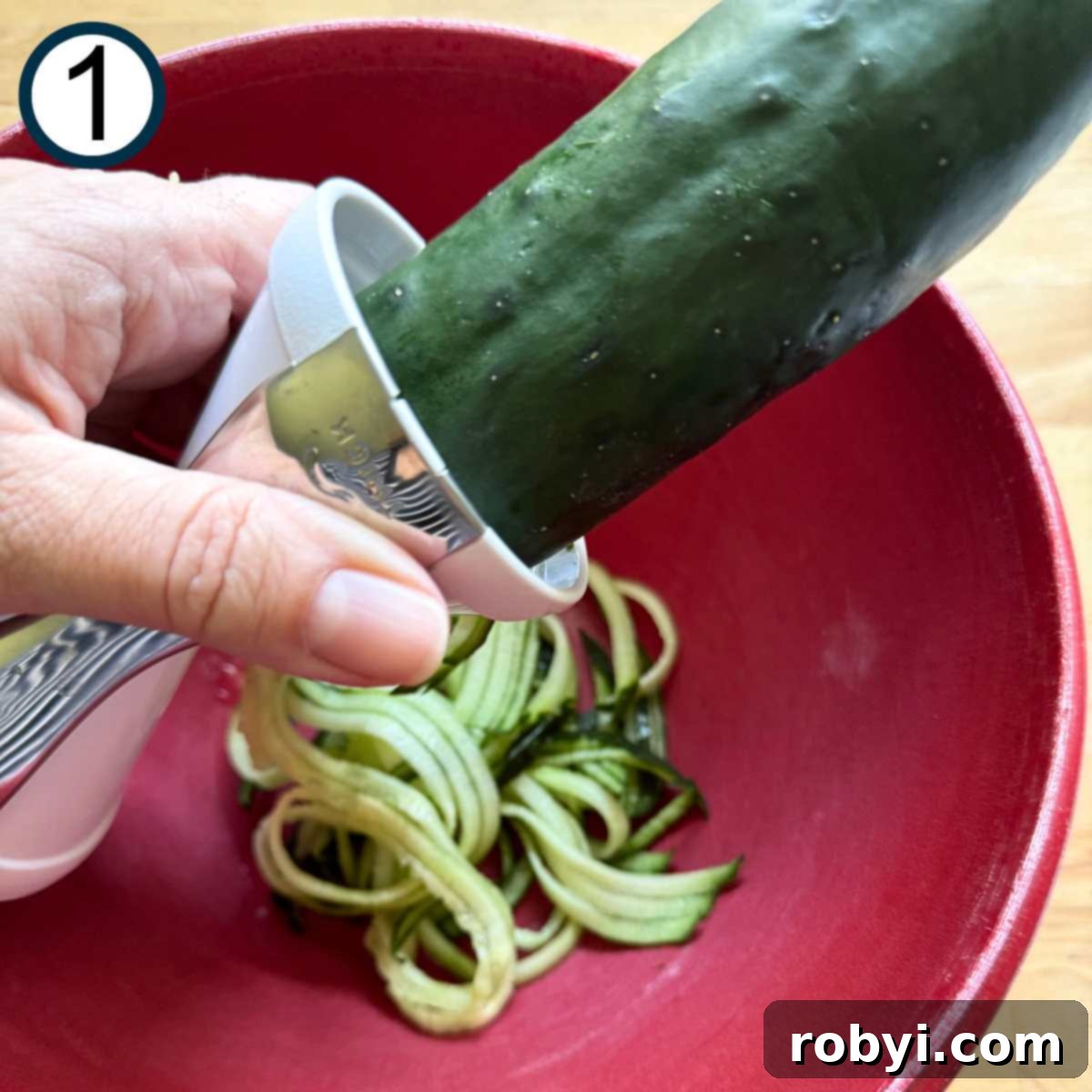 Cucumber being spiralized into a red bowl.