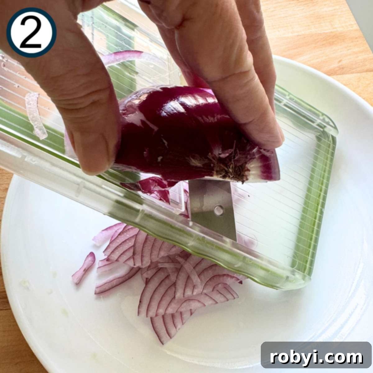 Red onion being sliced on a mandolin.