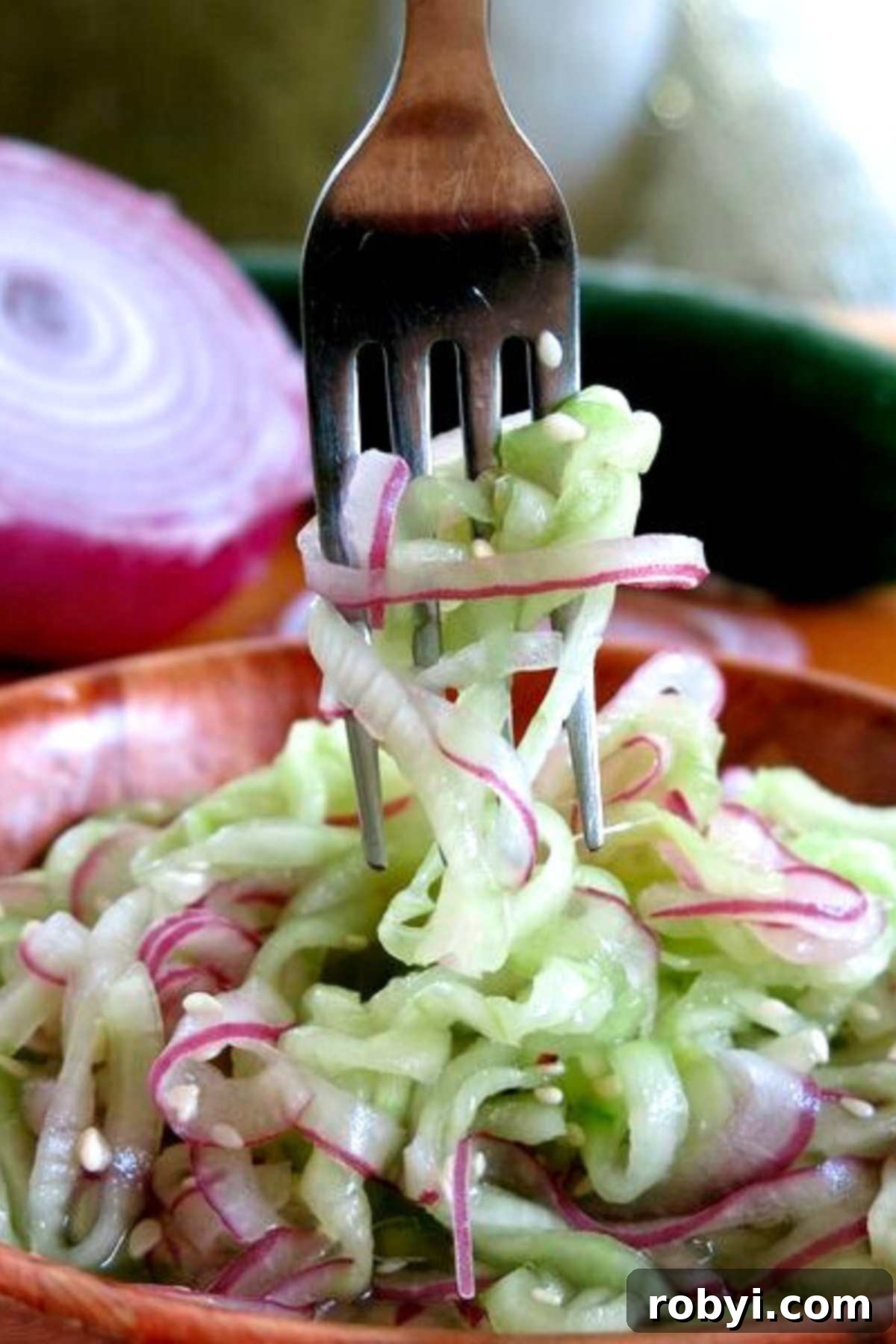 Fork pulling up spiralized cucumber and onion from the bowl with the salad.