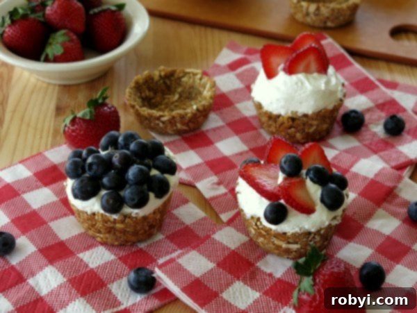 No-Bake Mini Cheesecakes topped with blueberries and strawberries, empty pretzel cups and bowls of berries for a topping bar