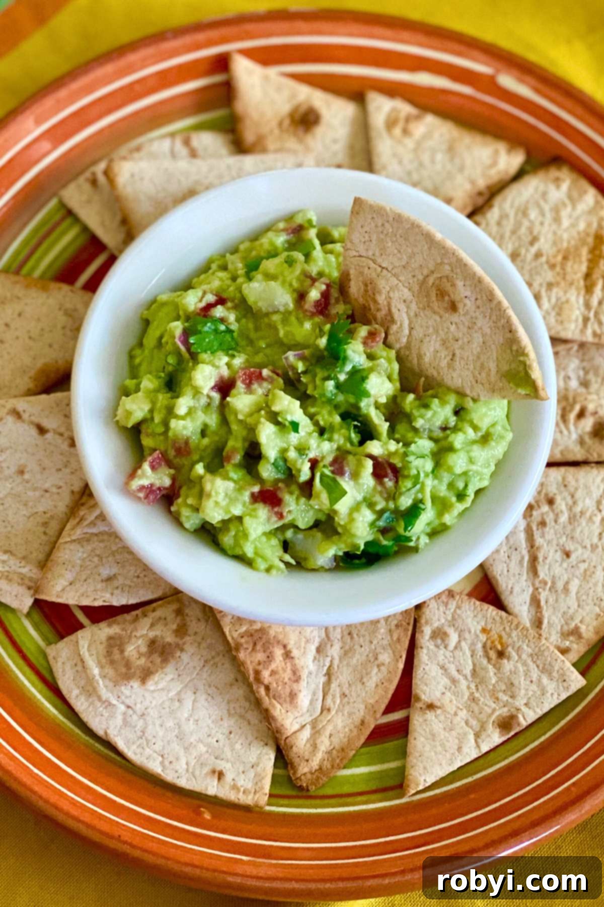 Chip dipped in bowl of guacamole dip with more chips surrounding it.