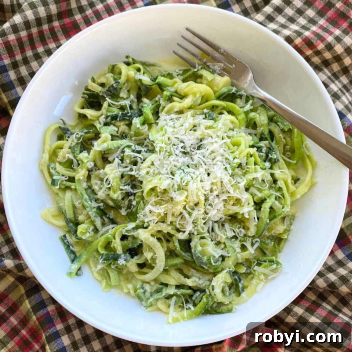 Creamy Zucchini Noodle Alfredo, garnished with fresh Parmesan cheese and a fork, ready to be enjoyed.