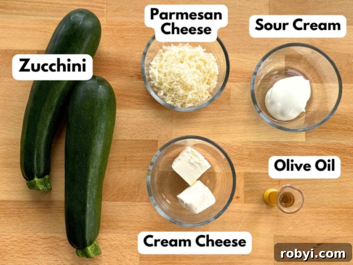 Array of fresh ingredients including zucchini, shredded Parmesan, sour cream, cream cheese cubes, and olive oil, laid out for an Alfredo recipe.