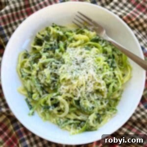 Zucchini noodle Alfredo topped with Parmesan cheese in a white bowl with a fork.