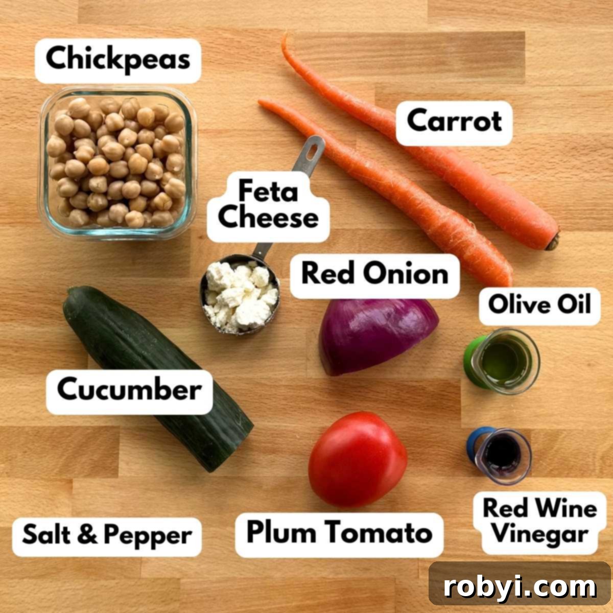 Labeled ingredients to make chickpea salad recipe: chickpeas, crumbled feta cheese, half an English cucumber, 2 carrots, plum tomato, red onion, olive oil, and red wine vinegar.