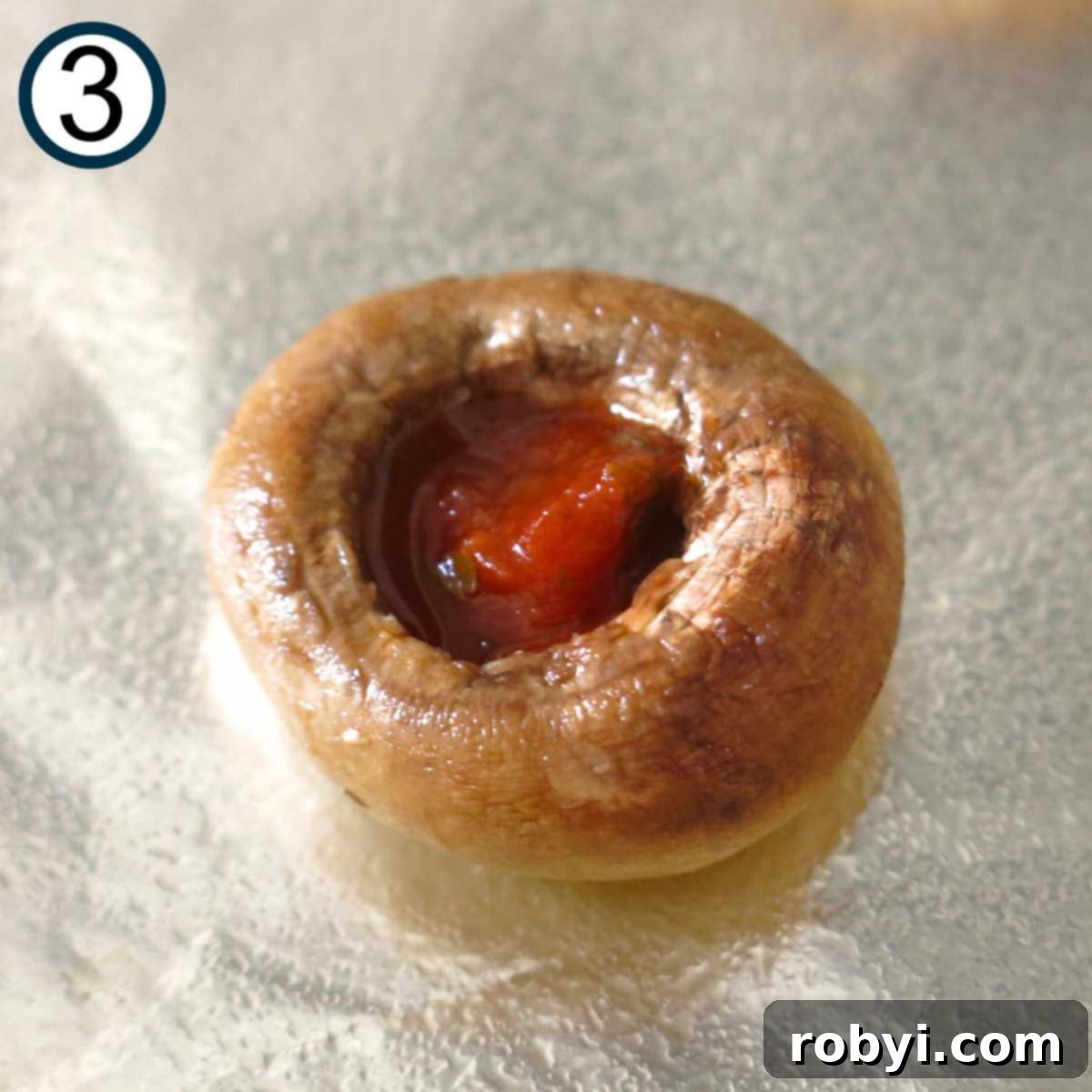 Close-up of a pre-baked button mushroom cap generously filled with vibrant red pizza sauce, ready for cheese and other toppings.