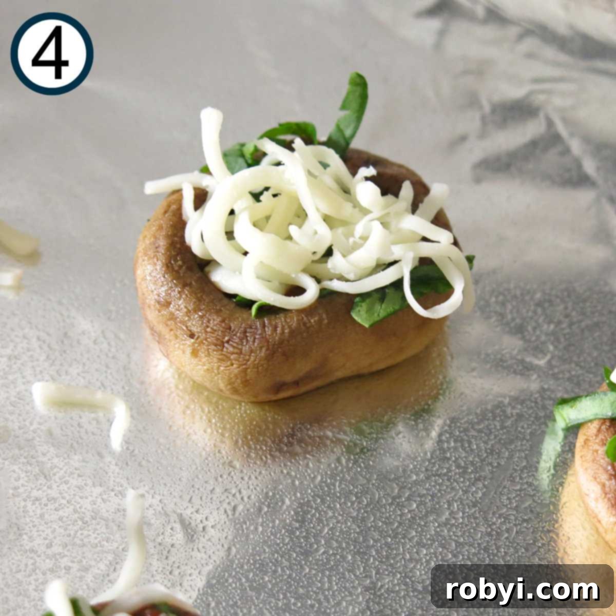 Close-up of a mushroom cap pizza bite, beautifully topped with finely chopped spinach and a generous layer of shredded mozzarella cheese, ready for broiling.
