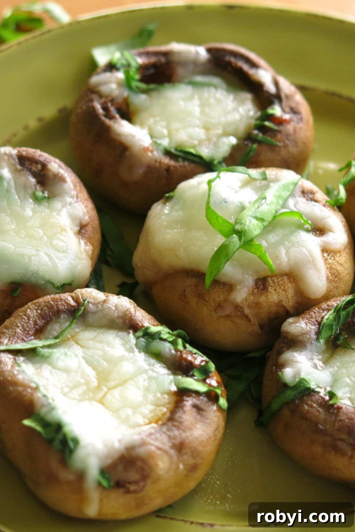 Five perfectly broiled Mushroom Cap Pizza Bites, adorned with melted mozzarella cheese and fresh green herbs, neatly arranged on a vibrant green serving plate.