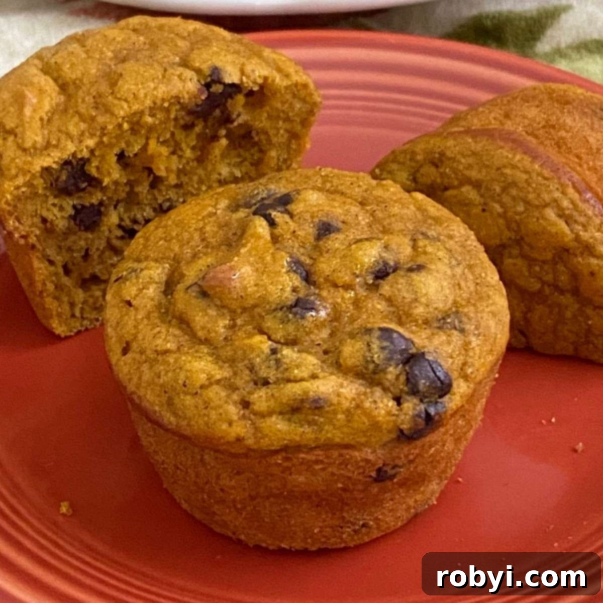 Two healthy Greek yogurt pumpkin muffins on a plate with one cut in half, showcasing their moist texture and golden color.