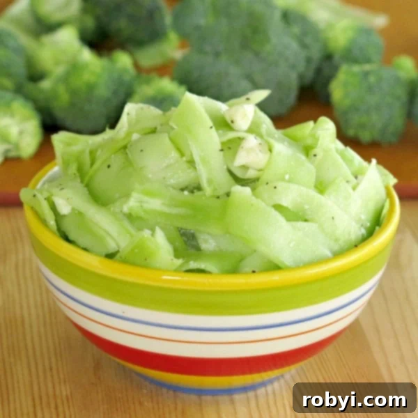 Vibrant raw broccoli stalk salad in a white bowl, garnished with crumbled feta cheese.