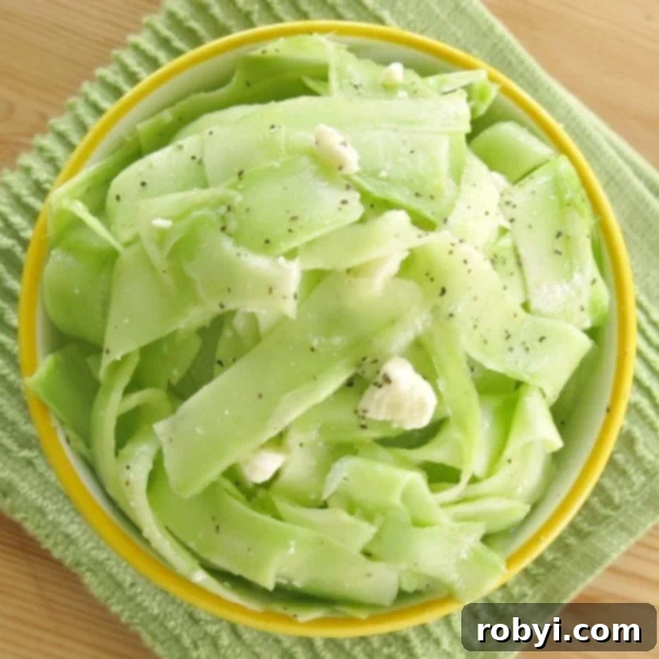 A close-up of the prepared broccoli stem salad in a stylish bowl, with dressing glistening on the ribbons.