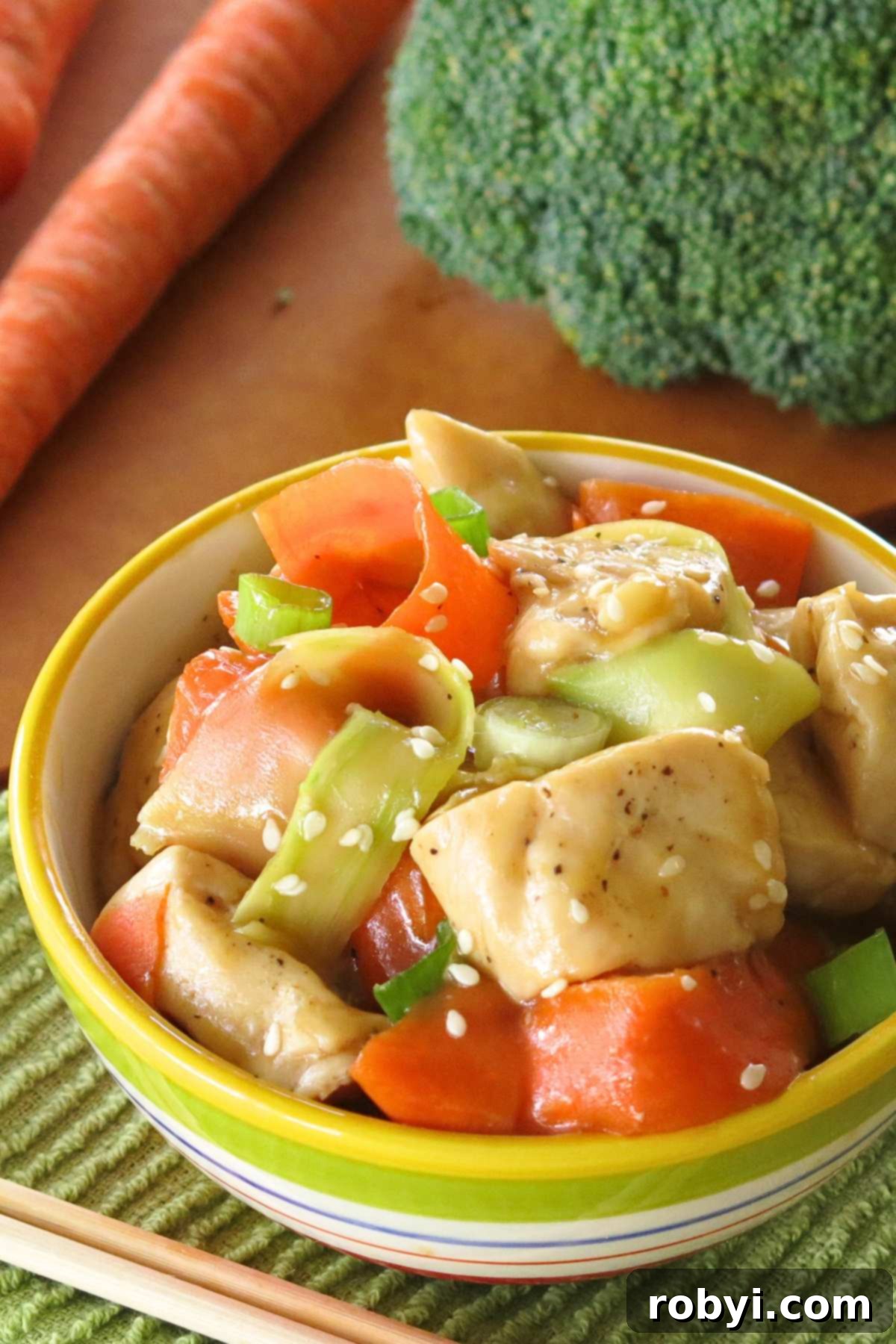 Fiery Orange Glazed Chicken 4 Healthy sweet and spicy orange chicken with shaved broccoli and carrots in bowl, with fresh broccoli and carrots in the background.