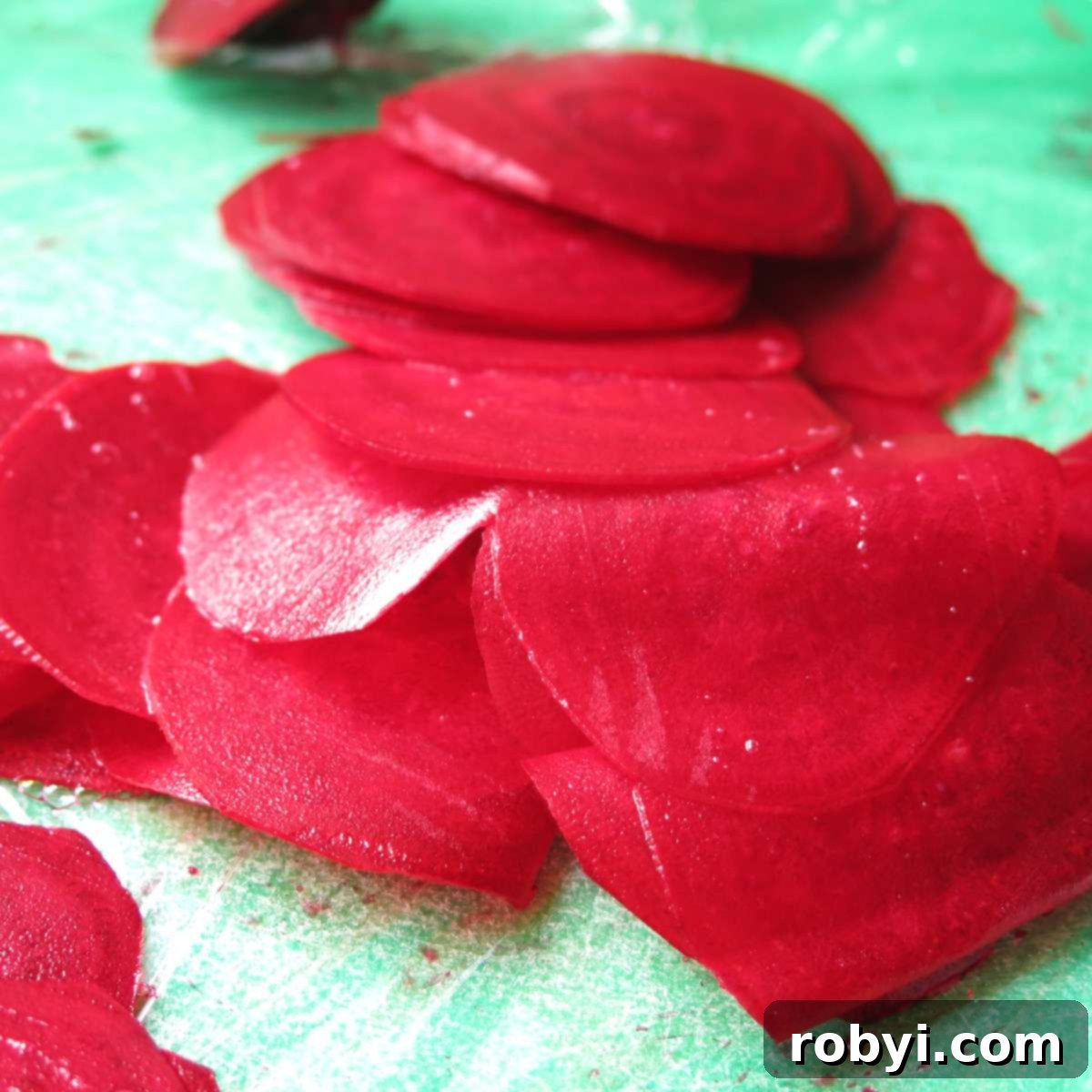 Thinly sliced raw beet rounds, approximately 1/16 inch thick, are neatly arranged on a wooden cutting board, ready for seasoning.