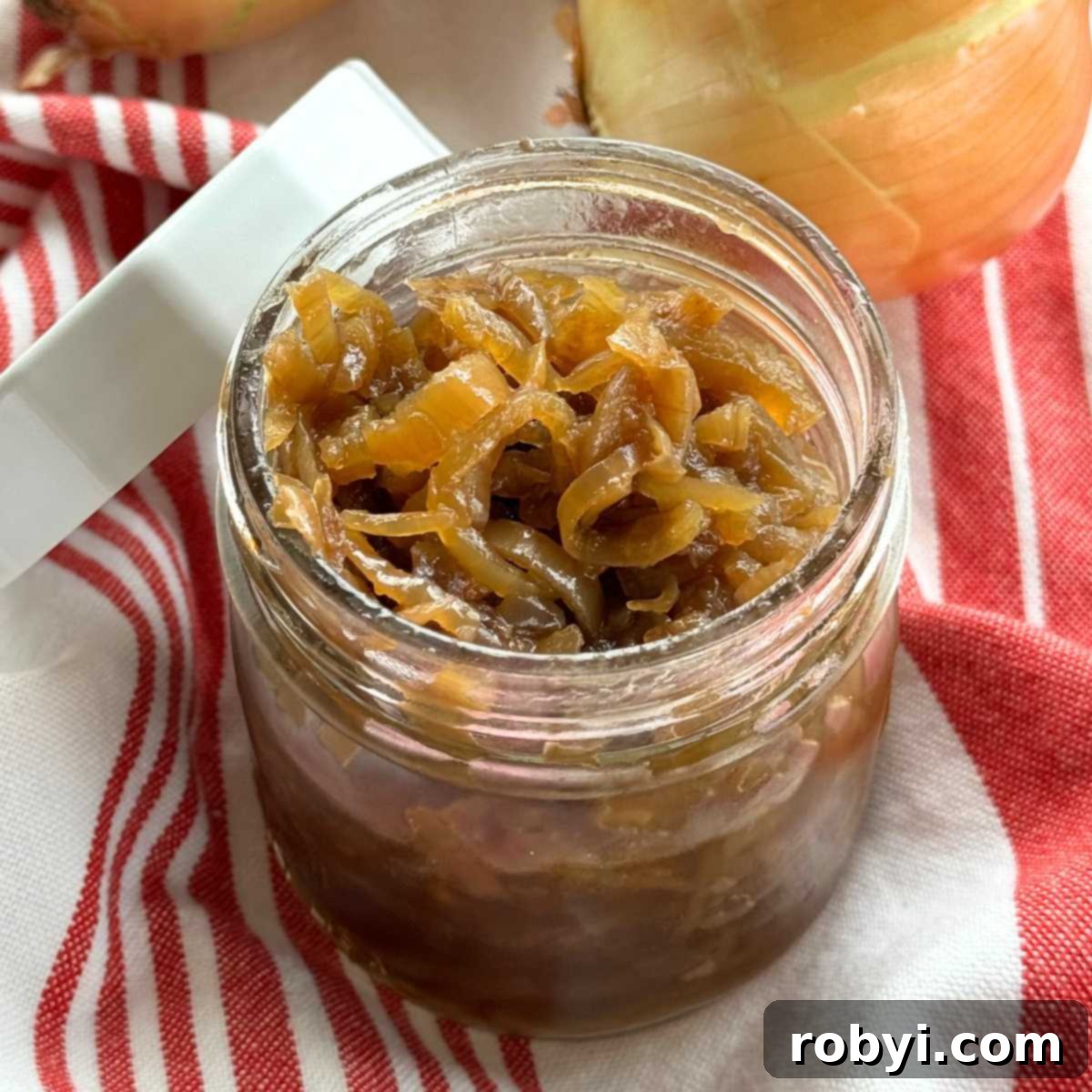 Slow cooker caramelized onions in a mason jar with fresh onions in the background, hinting at the transformation.