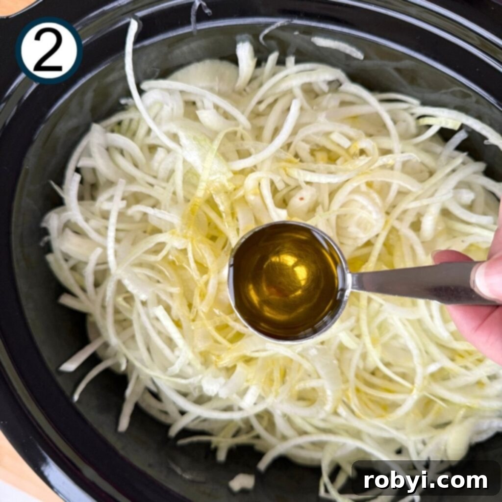 A spoon of olive oil being drizzled over a large quantity of sliced onions in a crock-pot.