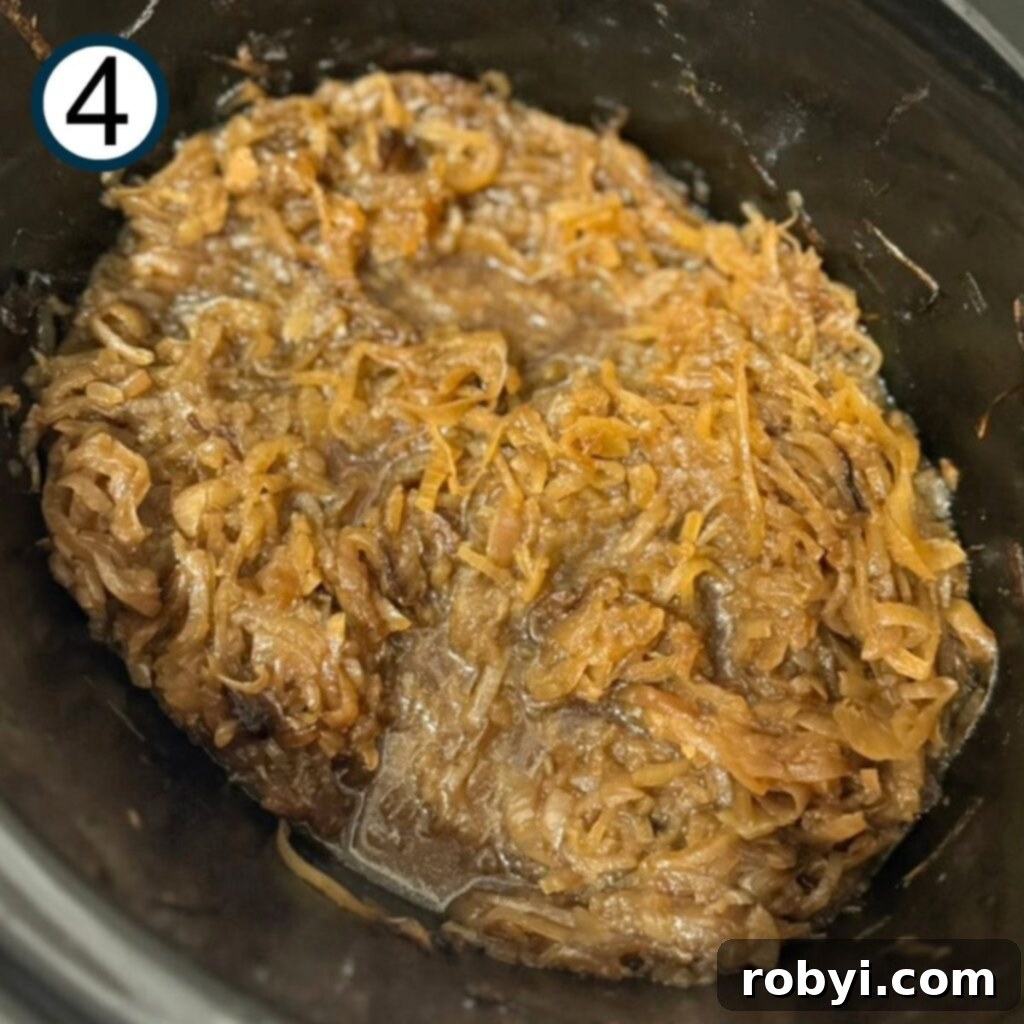Mostly cooked caramelized onions, deeply golden brown, in the insert of a slow cooker.