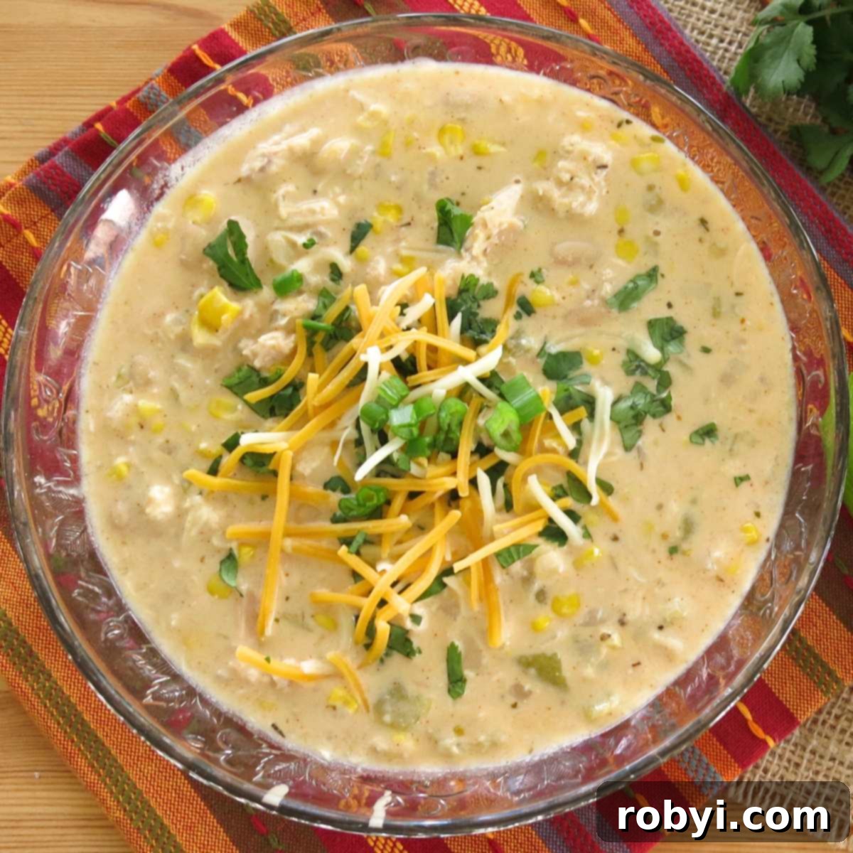 Cream Cheese Dream White Chicken Chili 2 Creamy white chicken chili made with cream cheese in a glass bowl topped with cilantro, green onions, and shredded cheese.