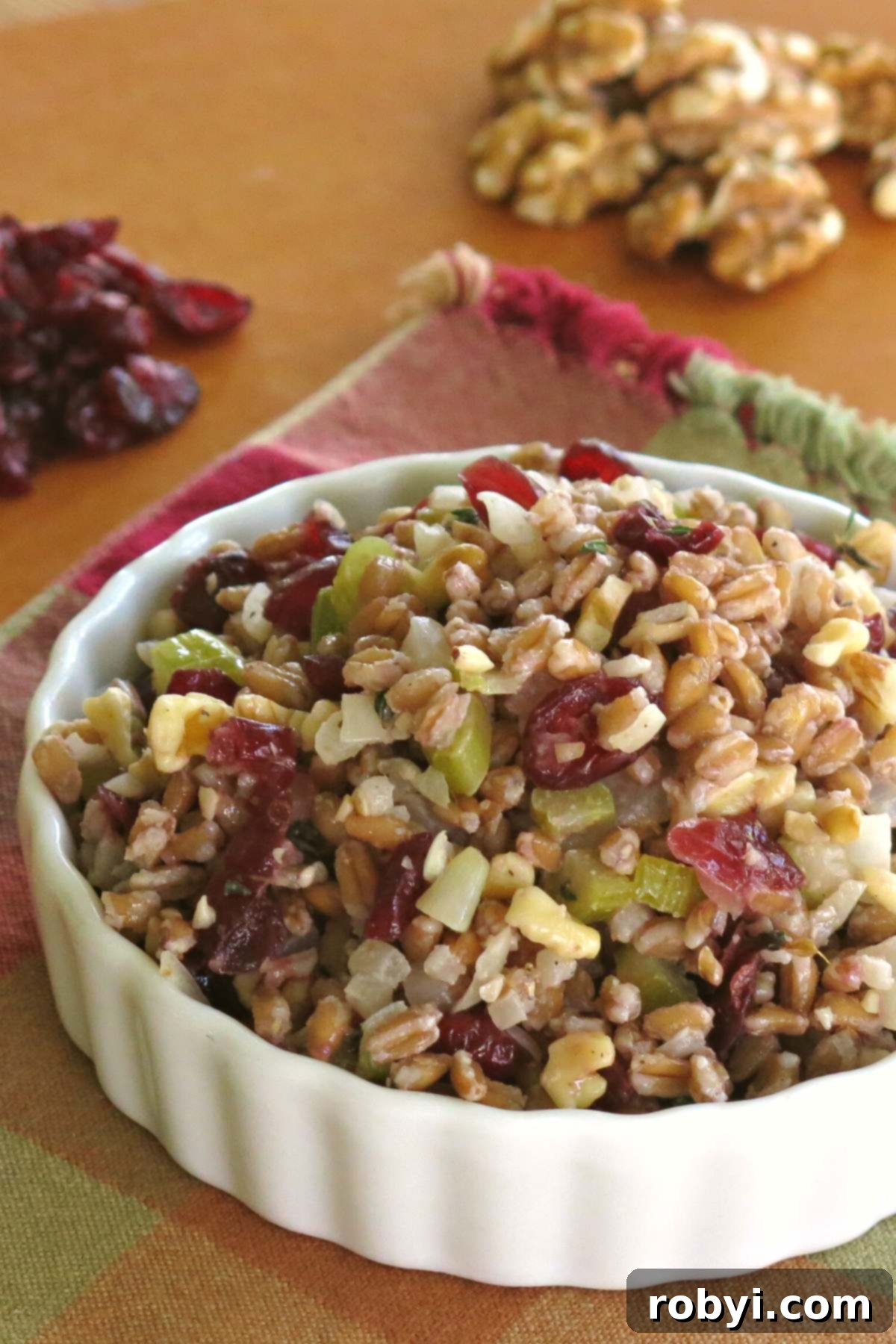 Farro Stuffing Pilaf in a serving bowl with walnuts and cranberries behind it.