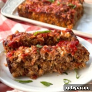Two slices of gourmet meatloaf with sundried tomatoes, mozzarella and Parmesan cheese, and oatmeal on a white plate with chopped basil, ready to serve.