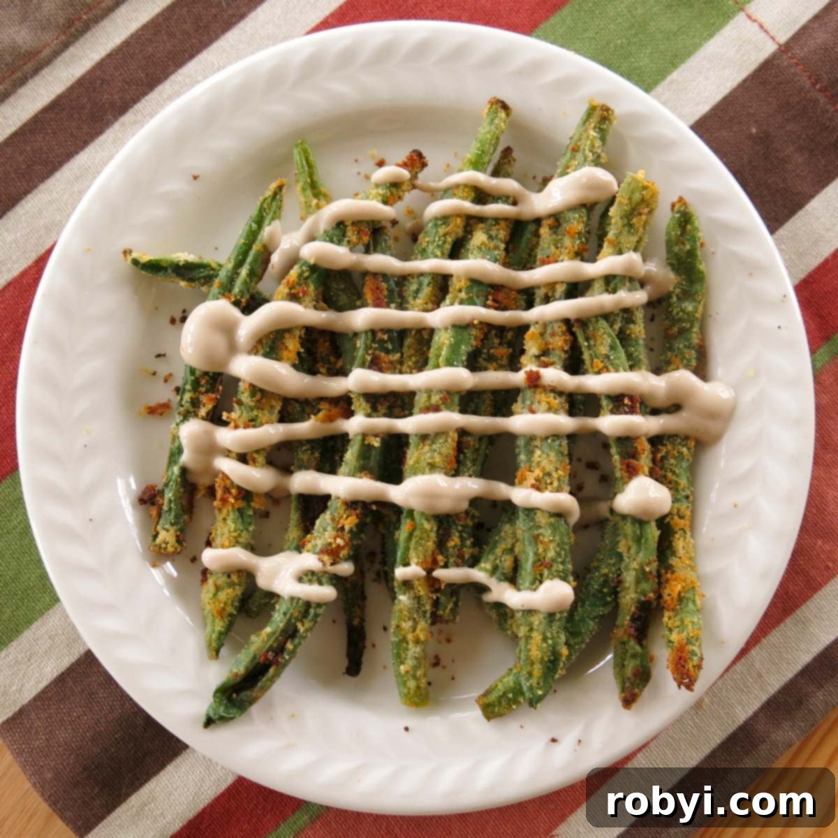Oven-Crisped Green Bean Fries 3 Keto green bean fries stacked on a plate with yogurt sauce drizzled over the top, showcasing elegant presentation.