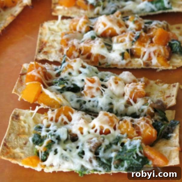 Slices of Butternut Squash Pizza with caramelized onion, fresh spinach, and melted mozzarella cheese, ready to be served, on a wooden board.