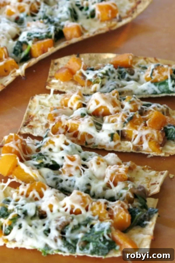 Close-up of a baked flatbread butternut squash pizza with melted cheese, fresh herbs, and a crispy crust.