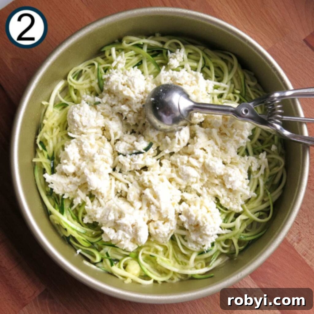 Naked Zucchini Noodle Tart 5 A spoon meticulously dropping dollops of the creamy three-cheese mixture (mozzarella, ricotta, Parmesan, and garlic) onto the zucchini noodle base in the baking dish.
