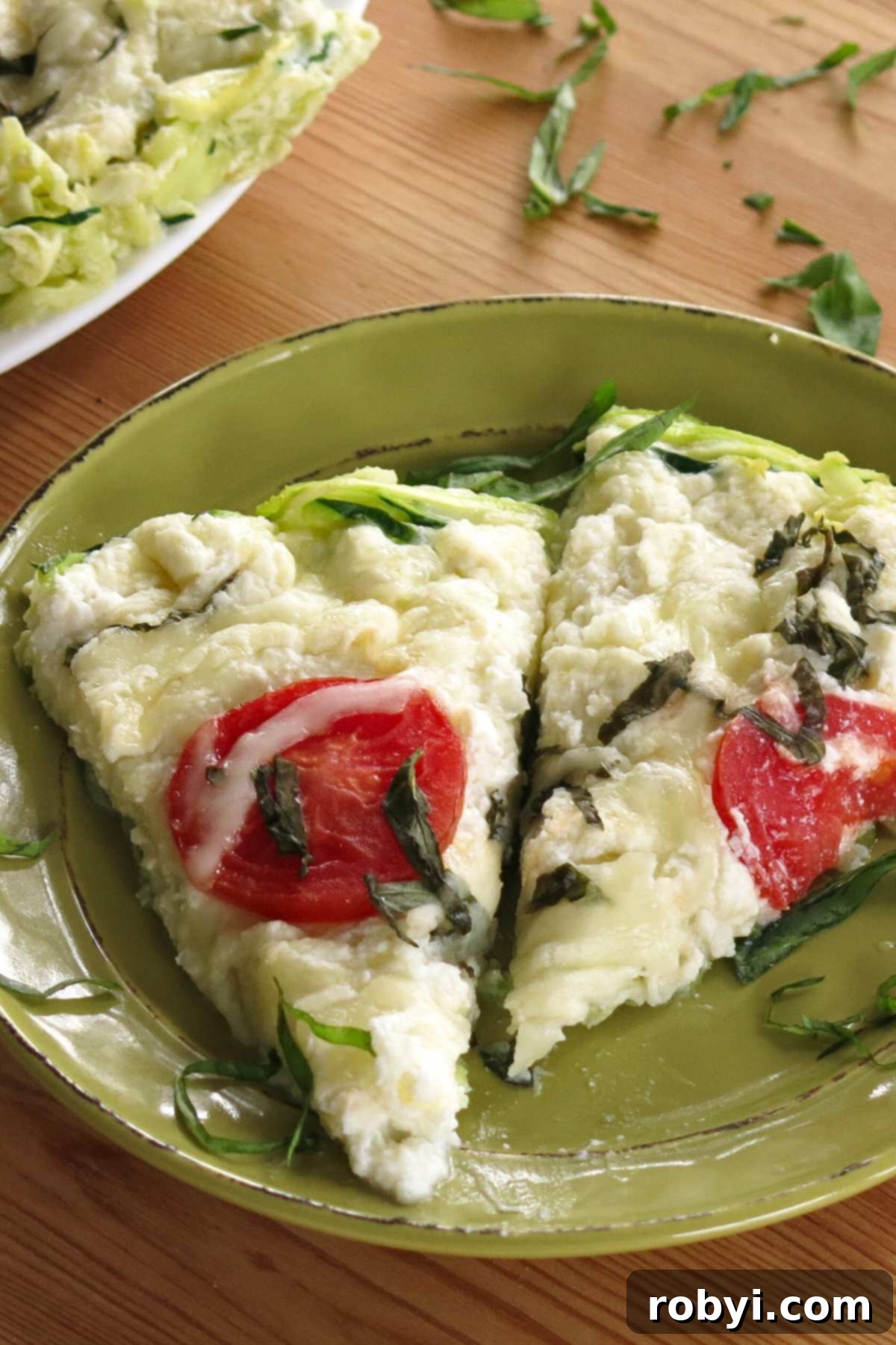 Naked Zucchini Noodle Tart 8 Two generous slices of crustless zucchini pie arranged on a vibrant green plate, with the rest of the pie in the baking dish and scattered fresh basil in the background.