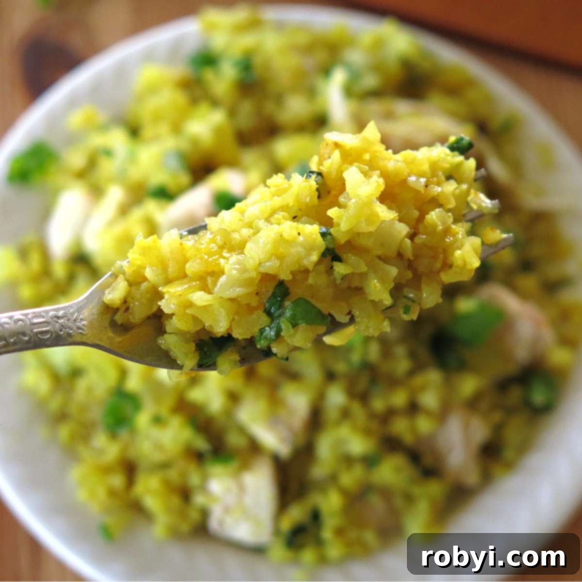Curry cauliflower rice on a fork with more in a bowl below it, showcasing its vibrant yellow color and fluffy texture.