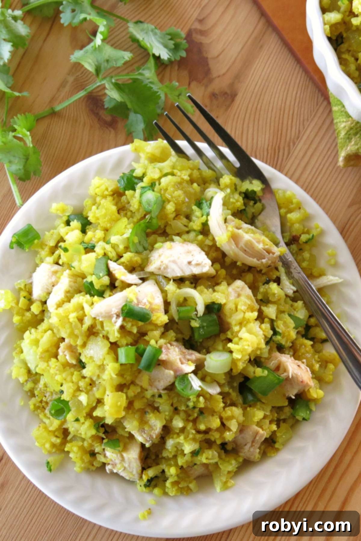 Curried cauliflower rice with pieces of baked lemon pepper chicken on top, garnished with fresh cilantro in the background.