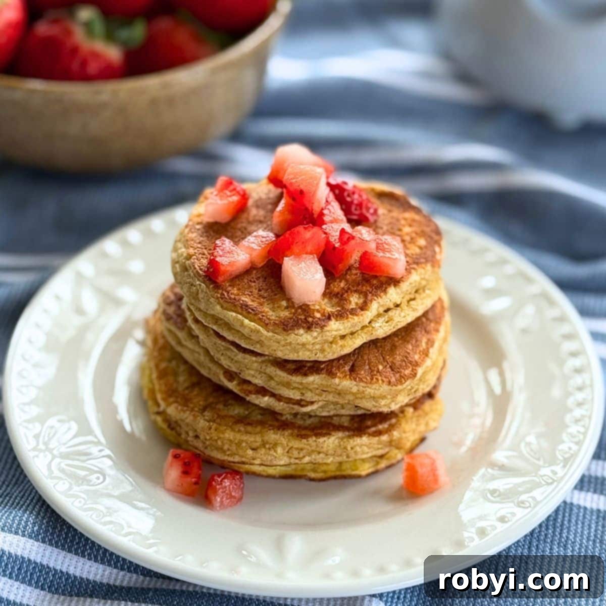 Stack of fluffy cottage cheese oat pancakes topped with fresh strawberries